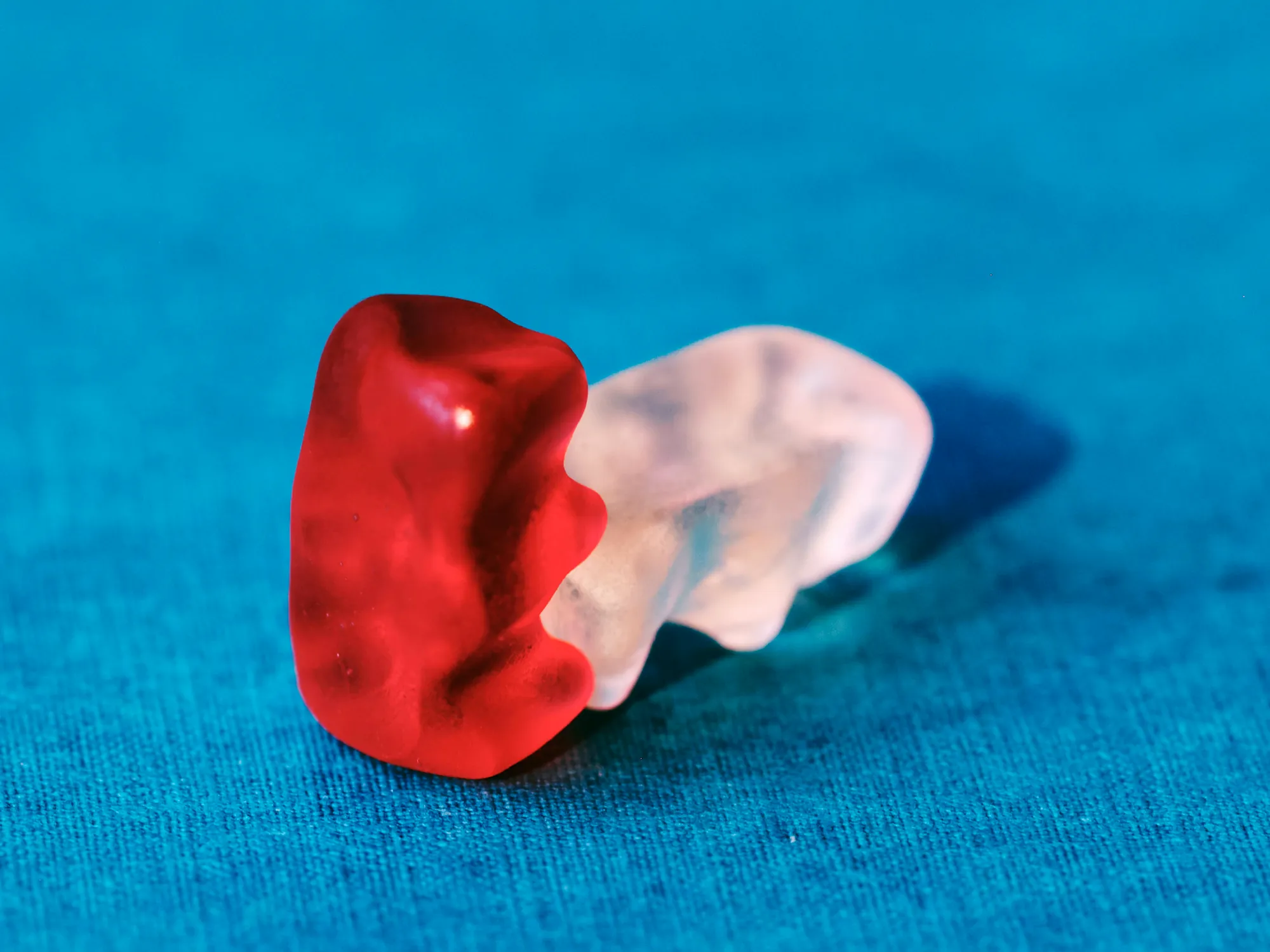 Un osito de goma rojo y uno transparente sobre fondo turquesa