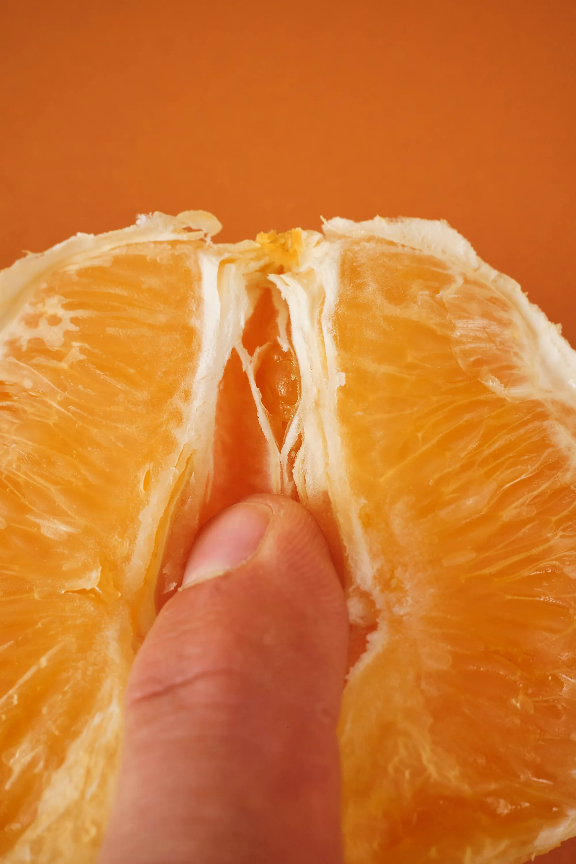 La yema de un dedo presionando el centro de una naranja partida